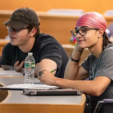 Two U N E students taking notes during a lecture in a lecture hall